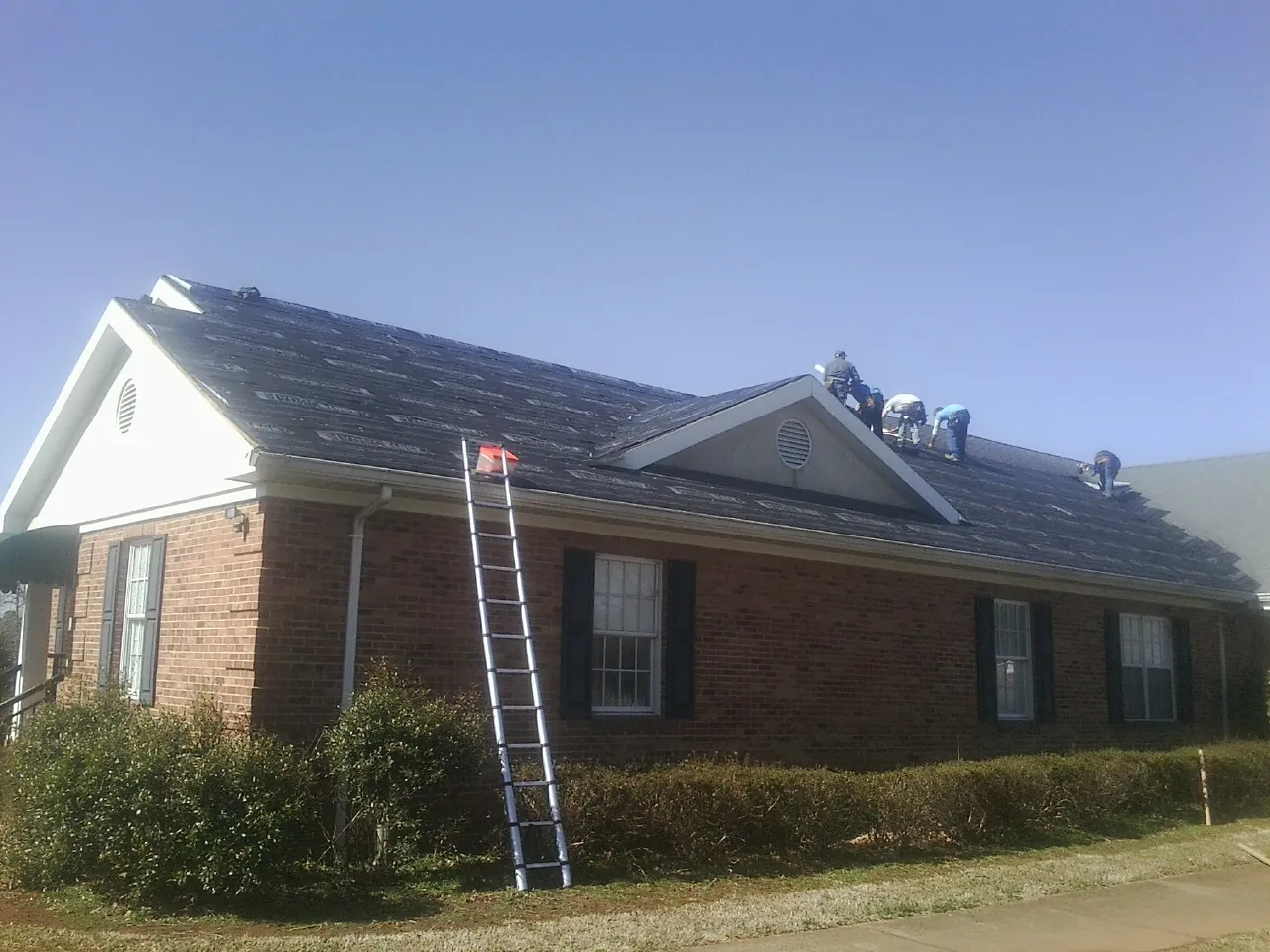 Crew tearing shingles off a brick ranch roof with a ladder set — Metal Roof Repair work by our crew in Huntingdon Valley