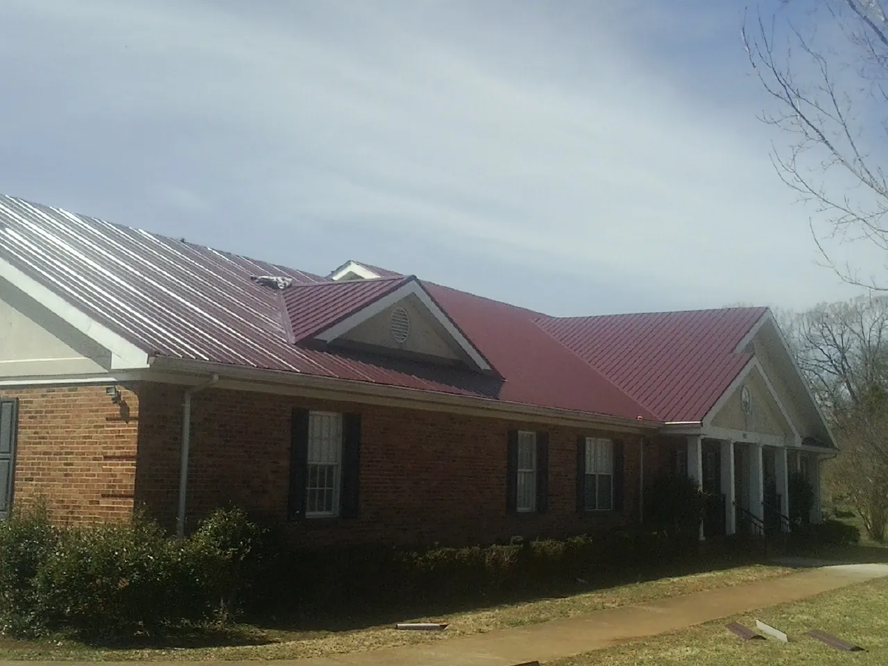 Red metal roof with gabled entries on a long brick building, from a Hail Damage Roof Repair job in Huntingdon Valley