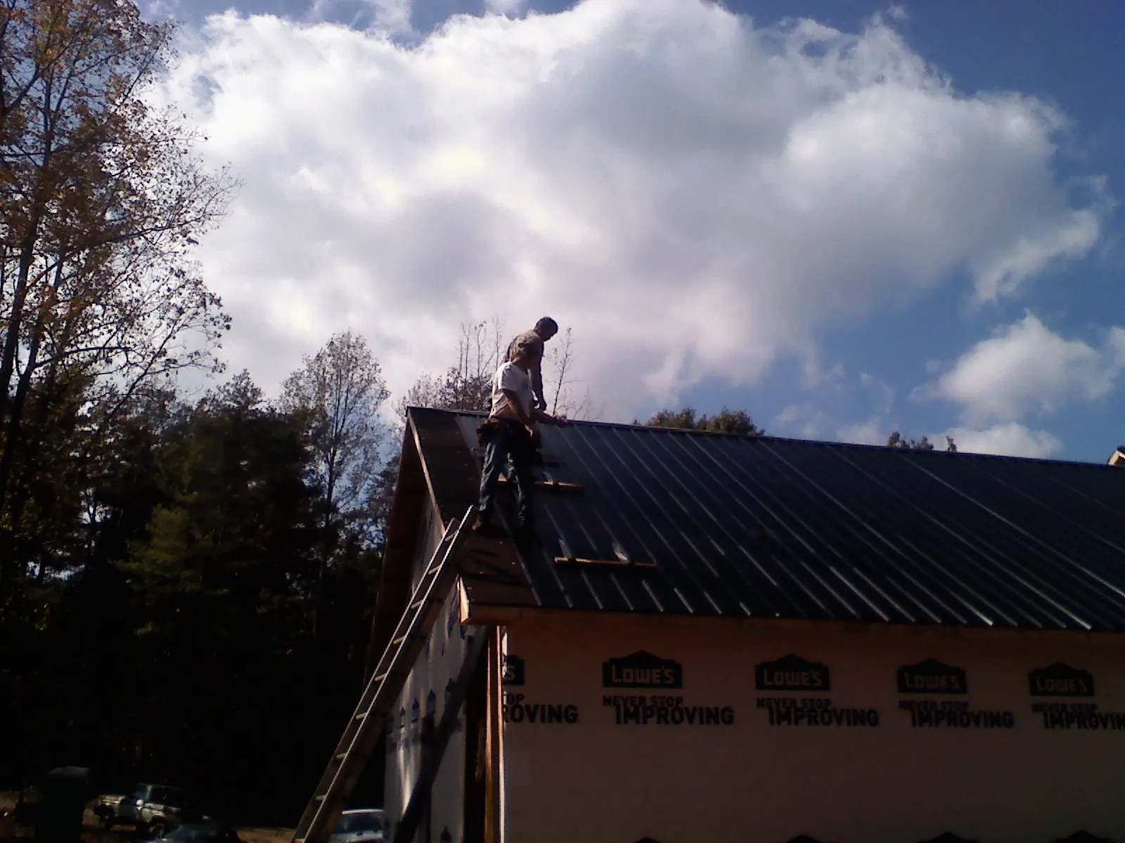 Roofer fastening dark metal panels high against a cloudy sky, from a Roof Inspection job in Huntingdon Valley