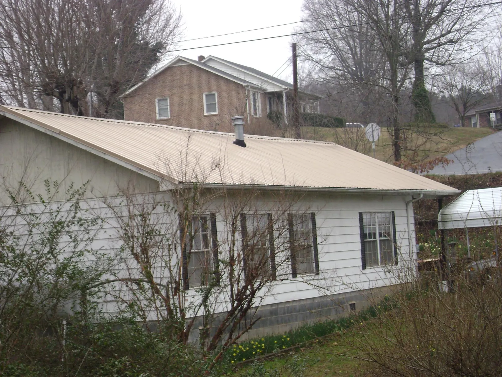 Tan metal roof on a white sided house set into a hillside — Commercial Roofing by Roofing Brothers in Huntingdon Valley